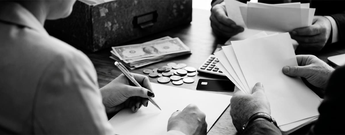 Advogados analisando documentos de uma cobrança bancária, com calculadora e dinheiro sobre a mesa